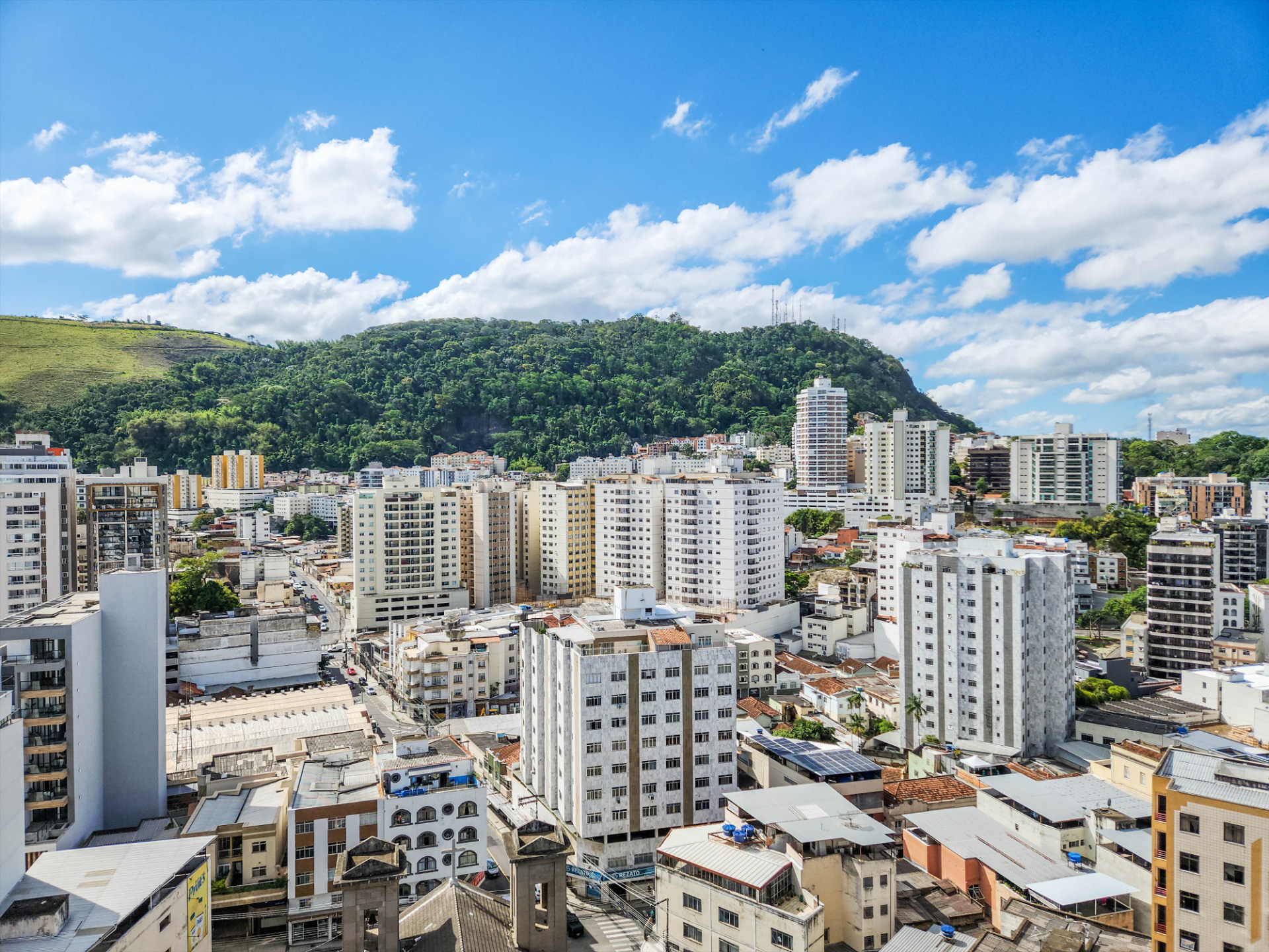 Vista aérea do centro de Juiz de Fora com prédios, morros e Mata Atlântica ao redor